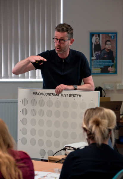 image of trainer talking to a group of trainees, holding a contrast sensitivity chart